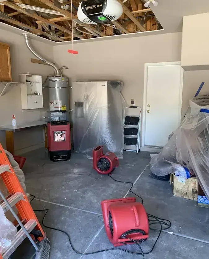 Air movers dry a garage beneath exposed ceiling framing and pipes