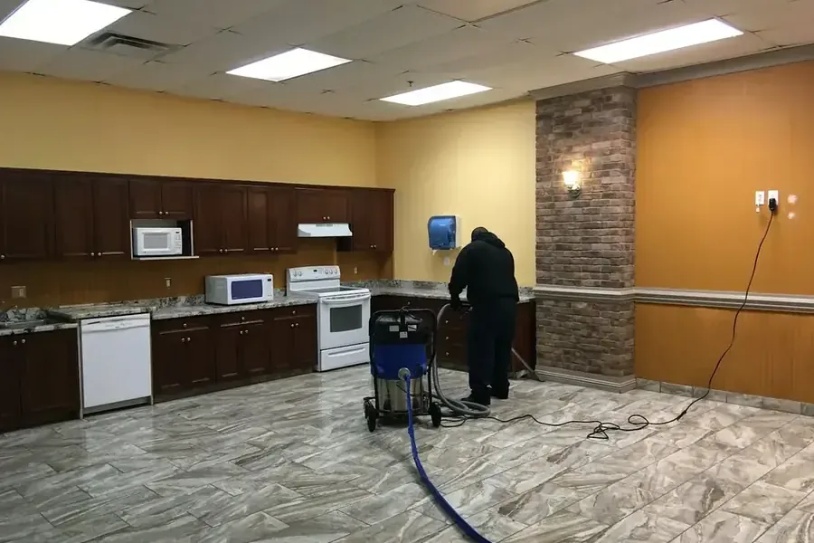 Technician using extraction equipment across a wet floor beside kitchen cabinets and appliances
