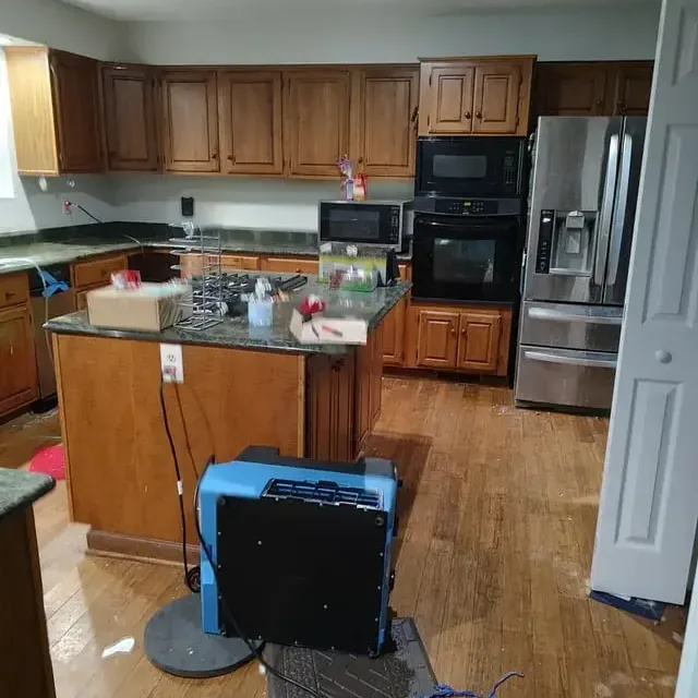 A blue dehumidifier stands on the hardwood floor of a furnished kitchen