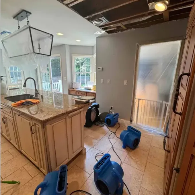 Blue air movers sit across the kitchen floor beneath an opened ceiling