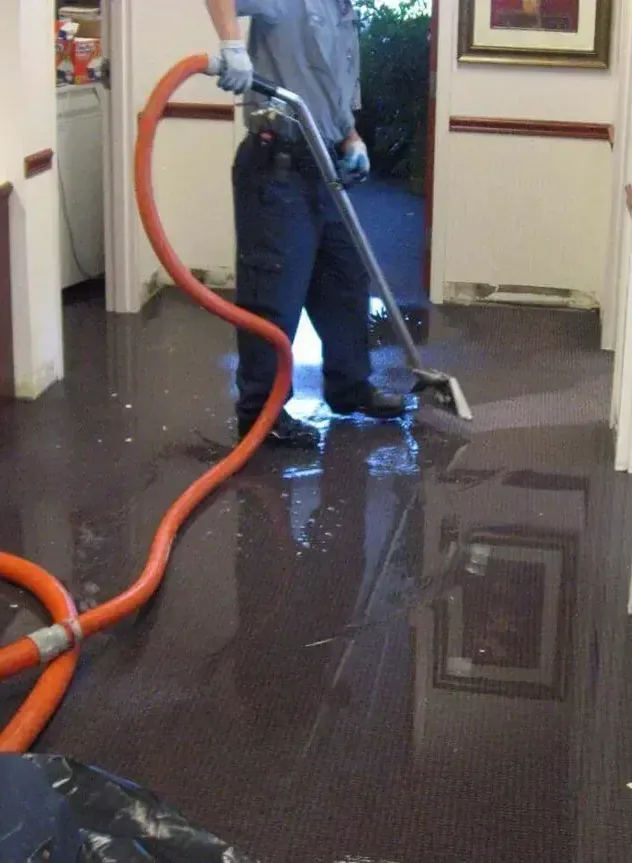 A technician uses an extraction wand and hose on a floor covered with standing water