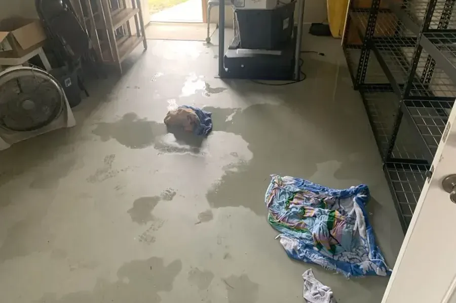 Puddles and wet towels spread across a garage floor beside stored equipment